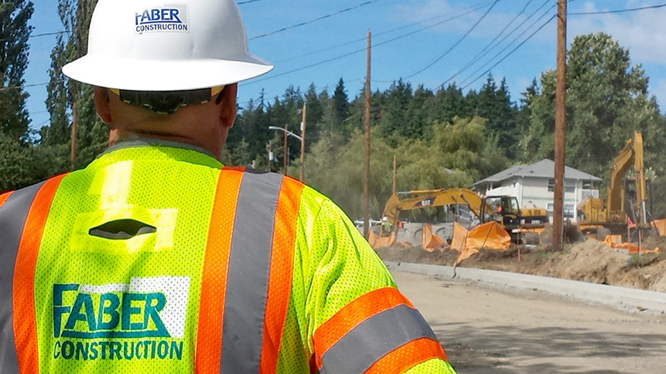 Faber Construction employee looking out at a construction site with heavy equipment Faber Construction employee looking out at a construction site with heavy equipment
